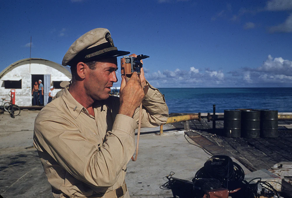 Slim Aaron in an American soldier's uniform, taking a photograph beside the sea.